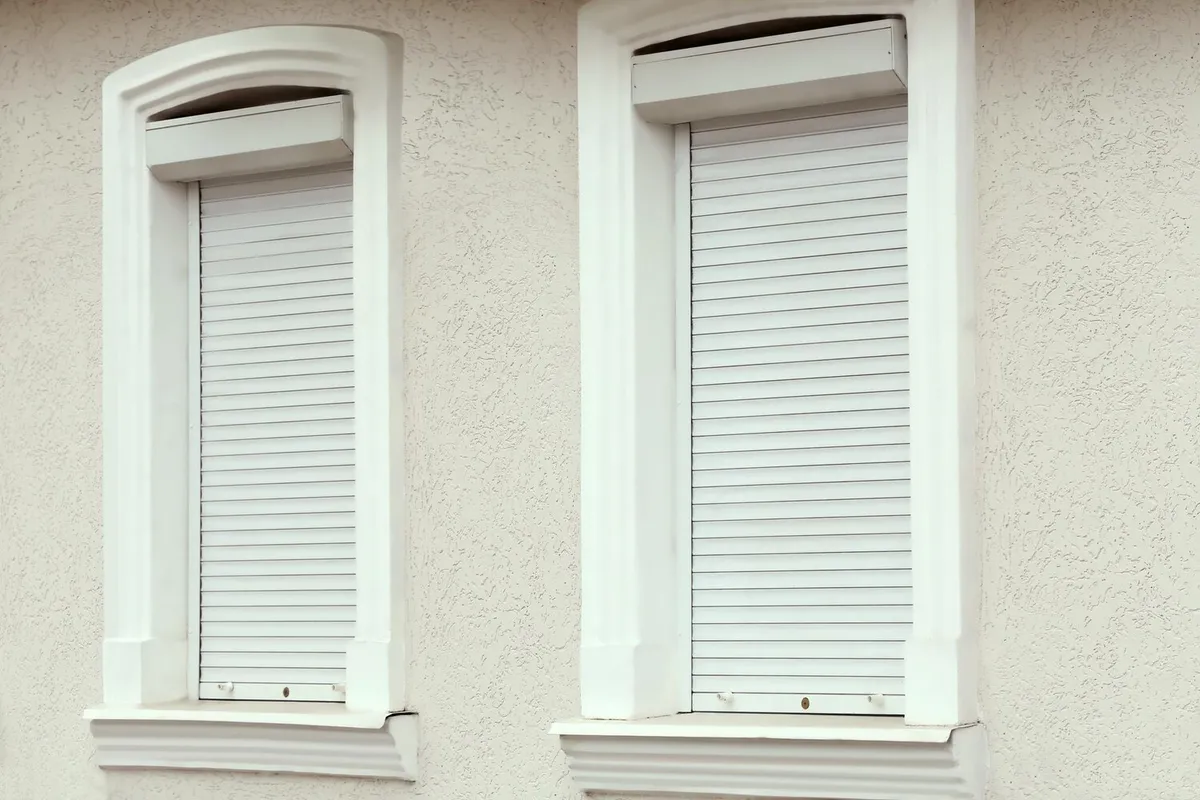 Deux fenêtres à encadrement mouluré équipées de volets roulants blancs à coffre de rénovation apparent, sur une façade enduite